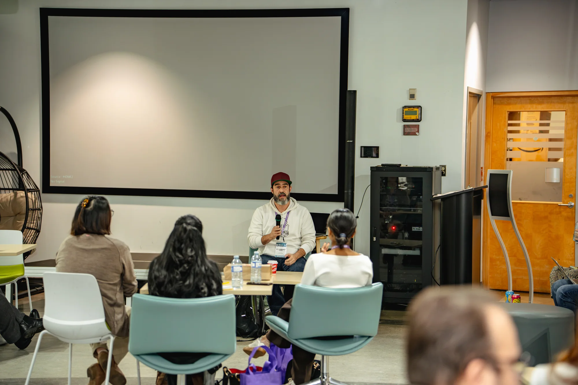A workshop speaker with a microphone and attendees seated at tables.